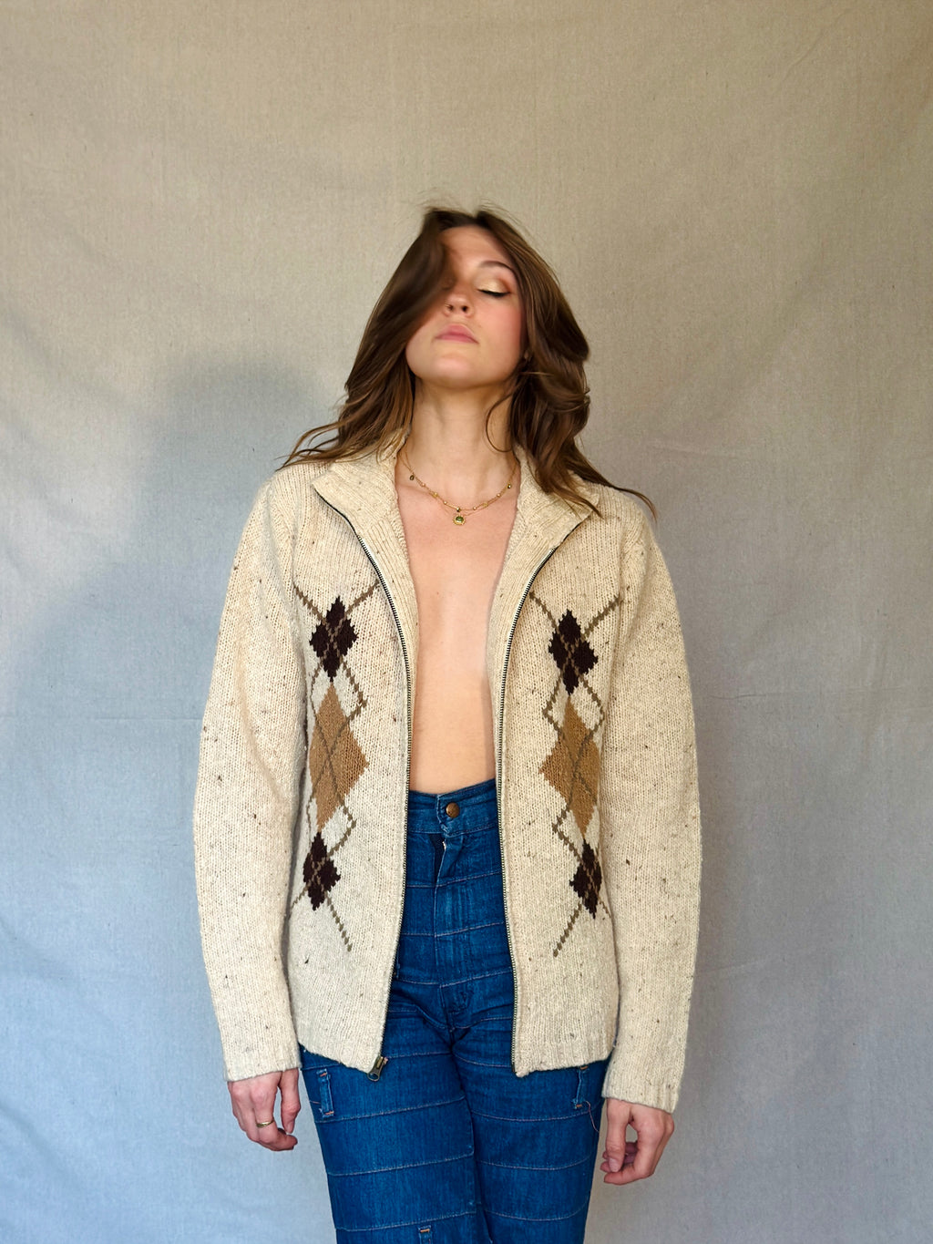 Woman wearing a cream argyle cardigan over a blue top against a plain background