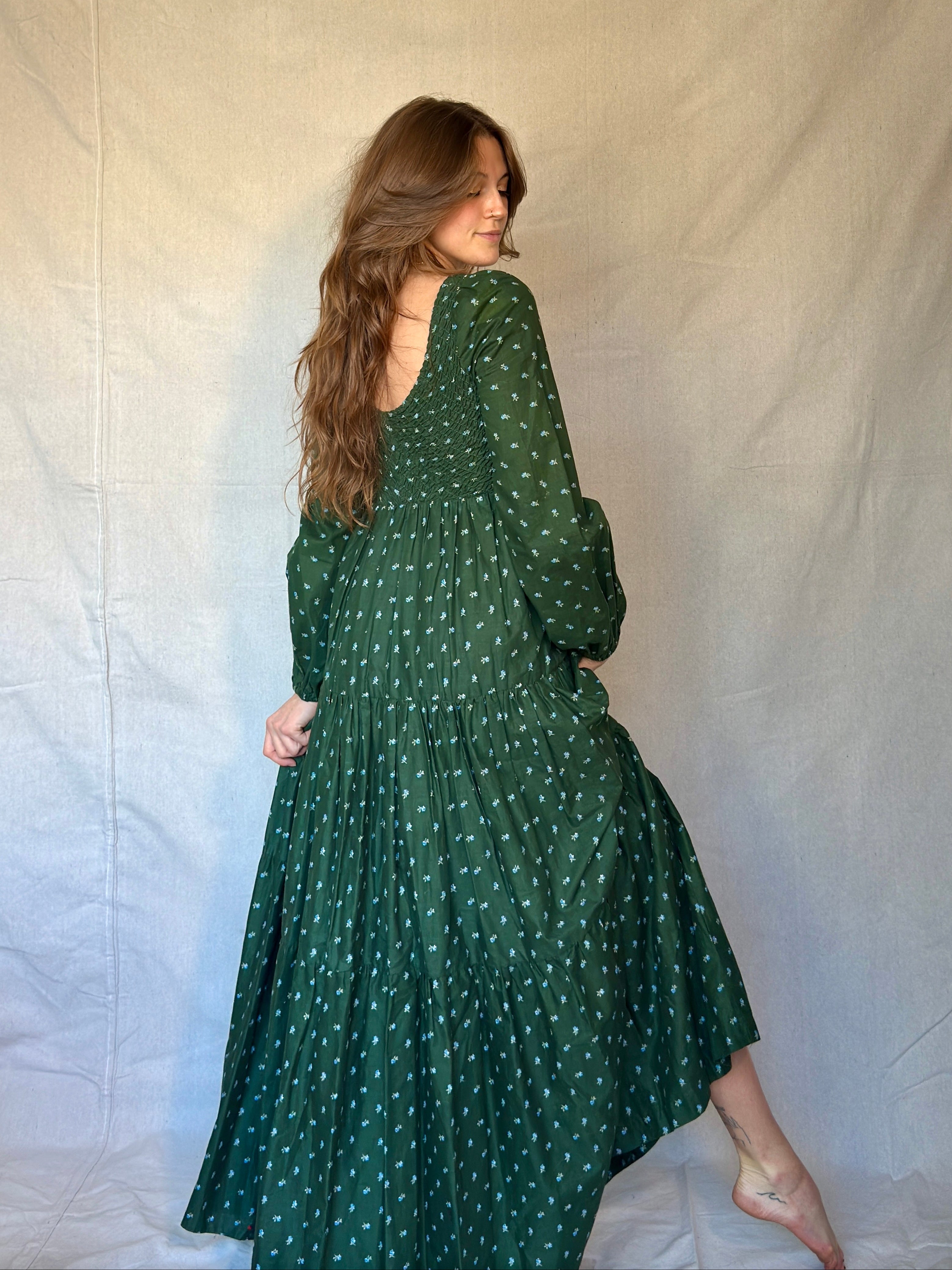 Woman wearing a green tiered prairie dress with blue and white micro floral pattern against a plain background