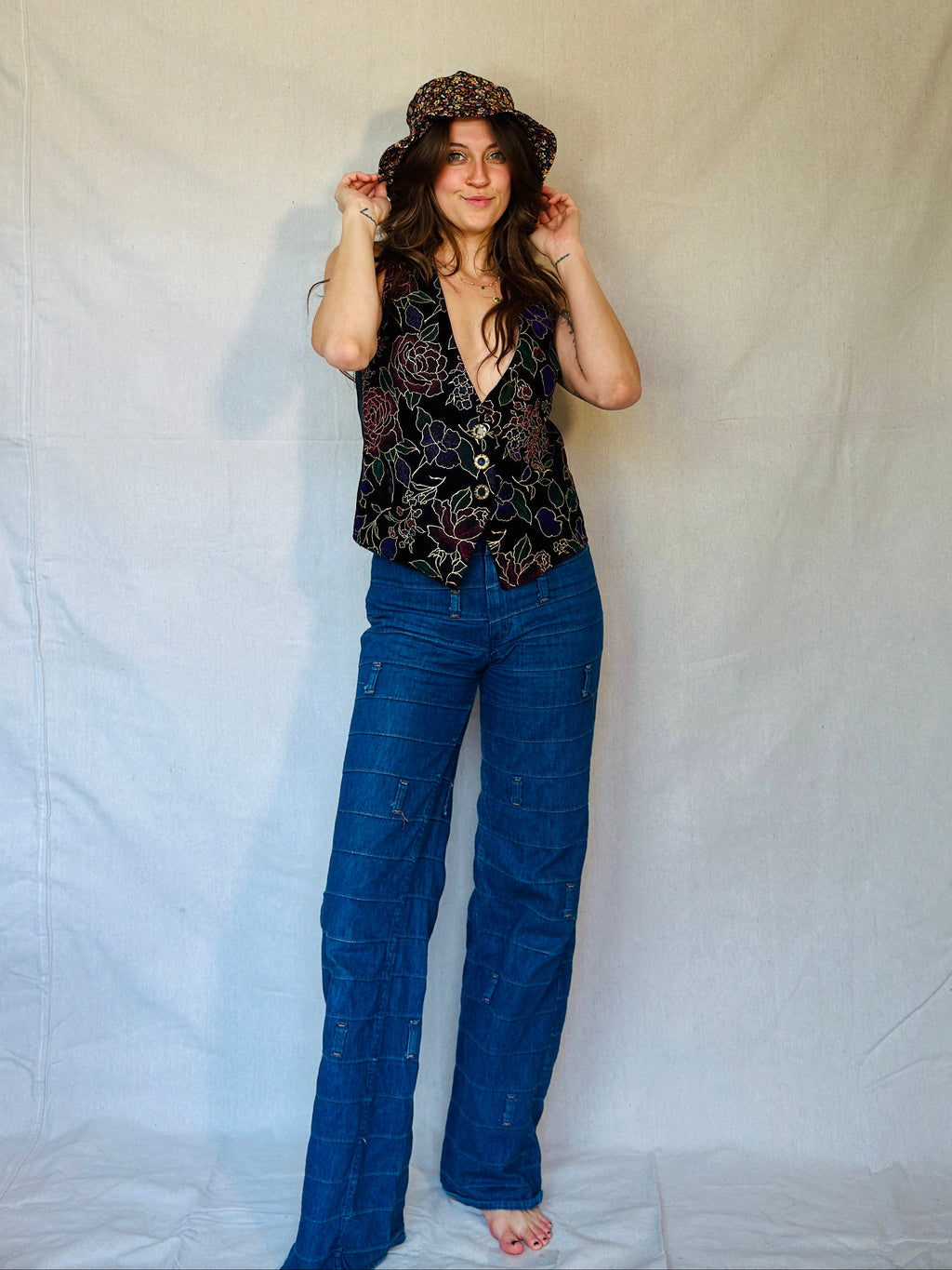 Woman wearing a patterned top and blue jeans against a plain background
