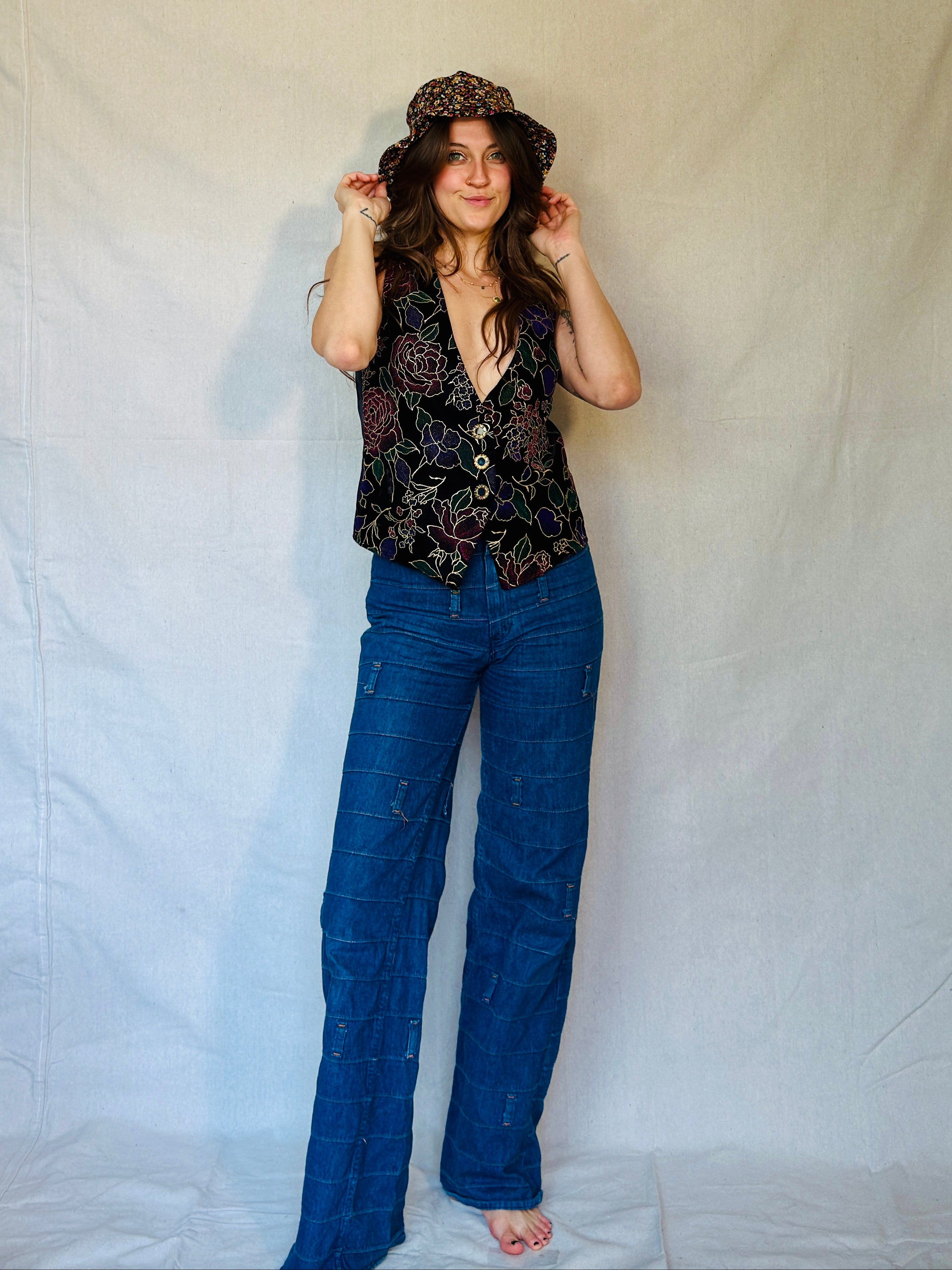 Woman wearing a patterned top and blue jeans against a plain background