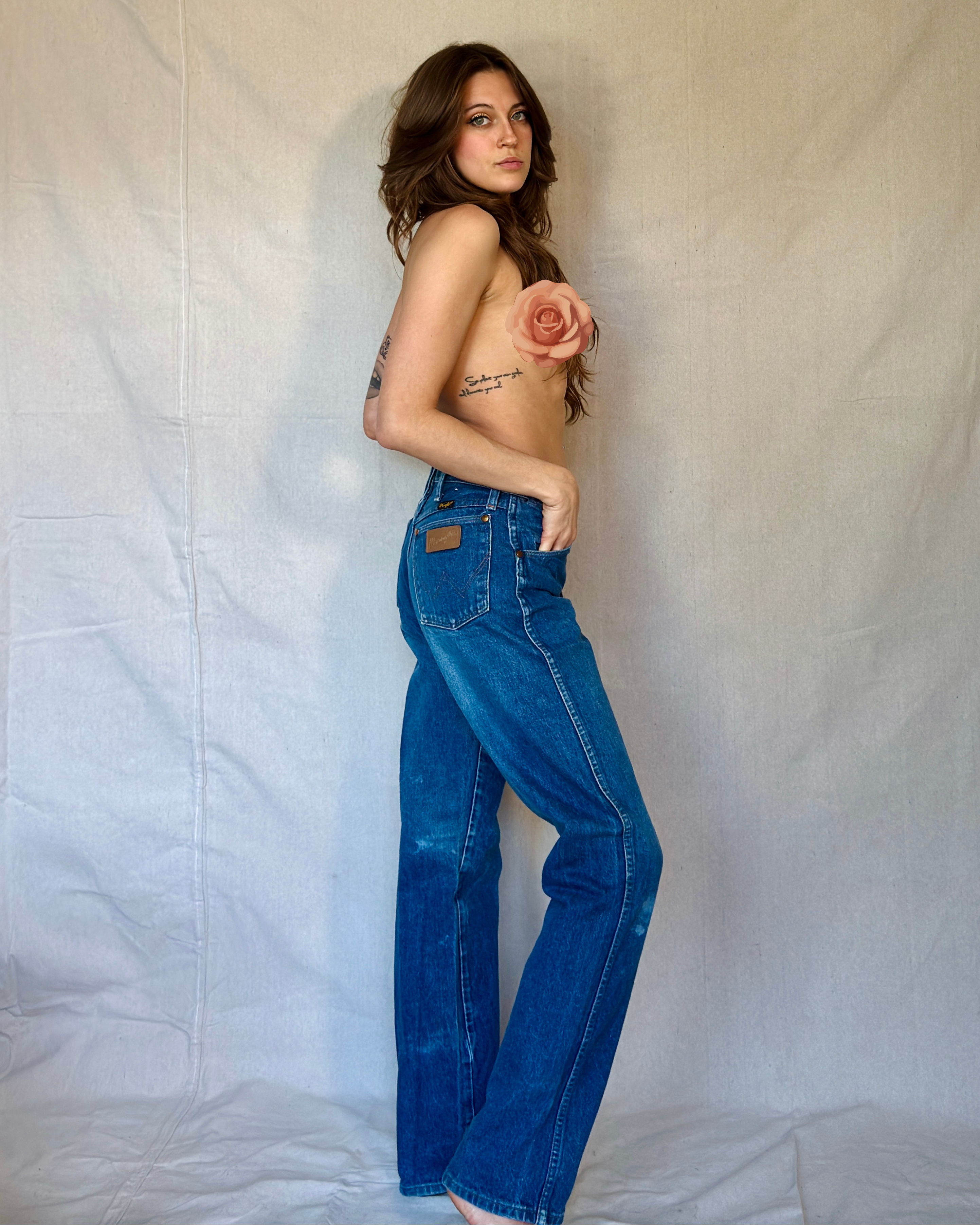 Person wearing blue jeans holding a rose against a plain background