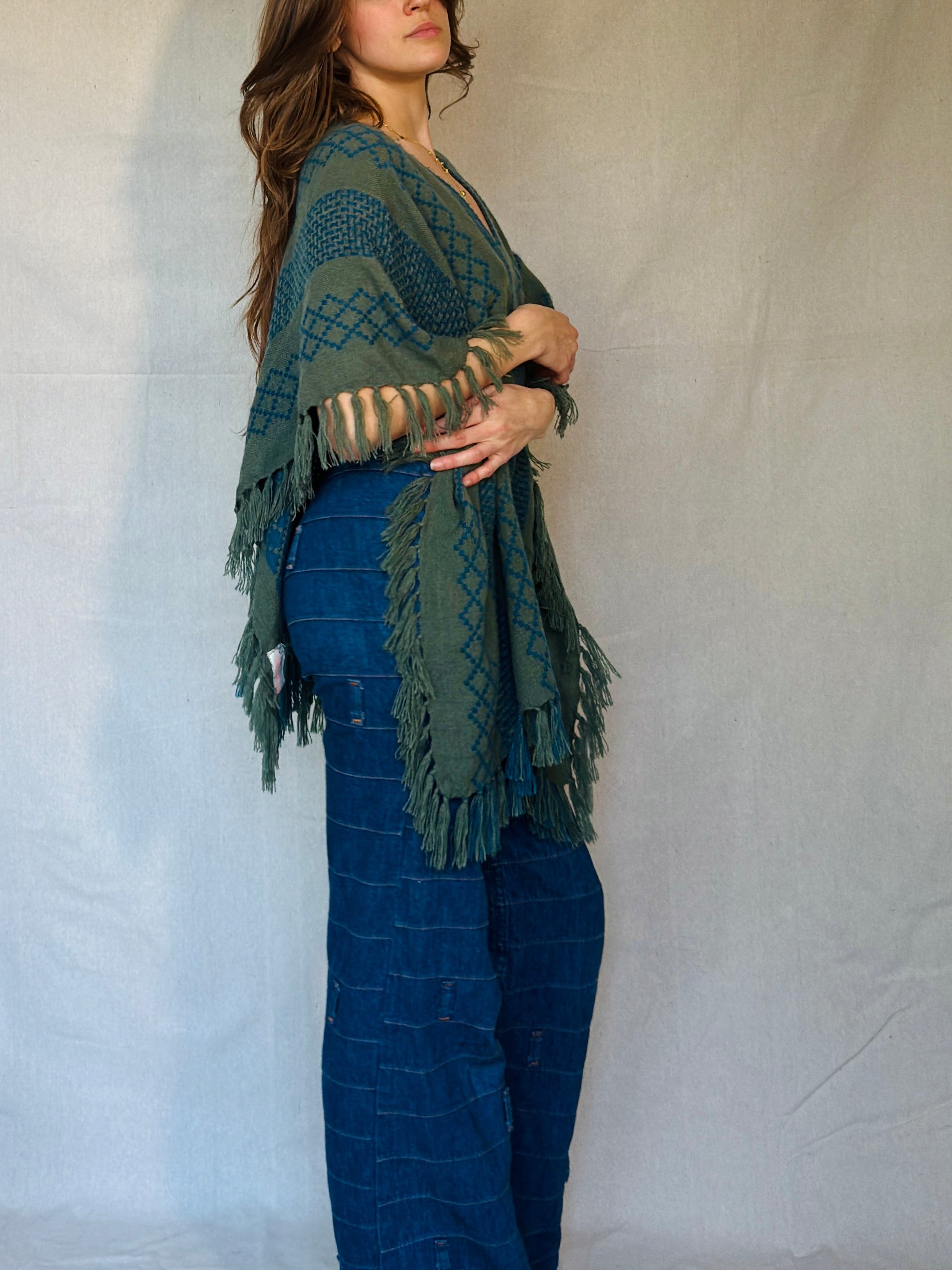 Woman wearing a green knitted shawl over a blue outfit against a plain background