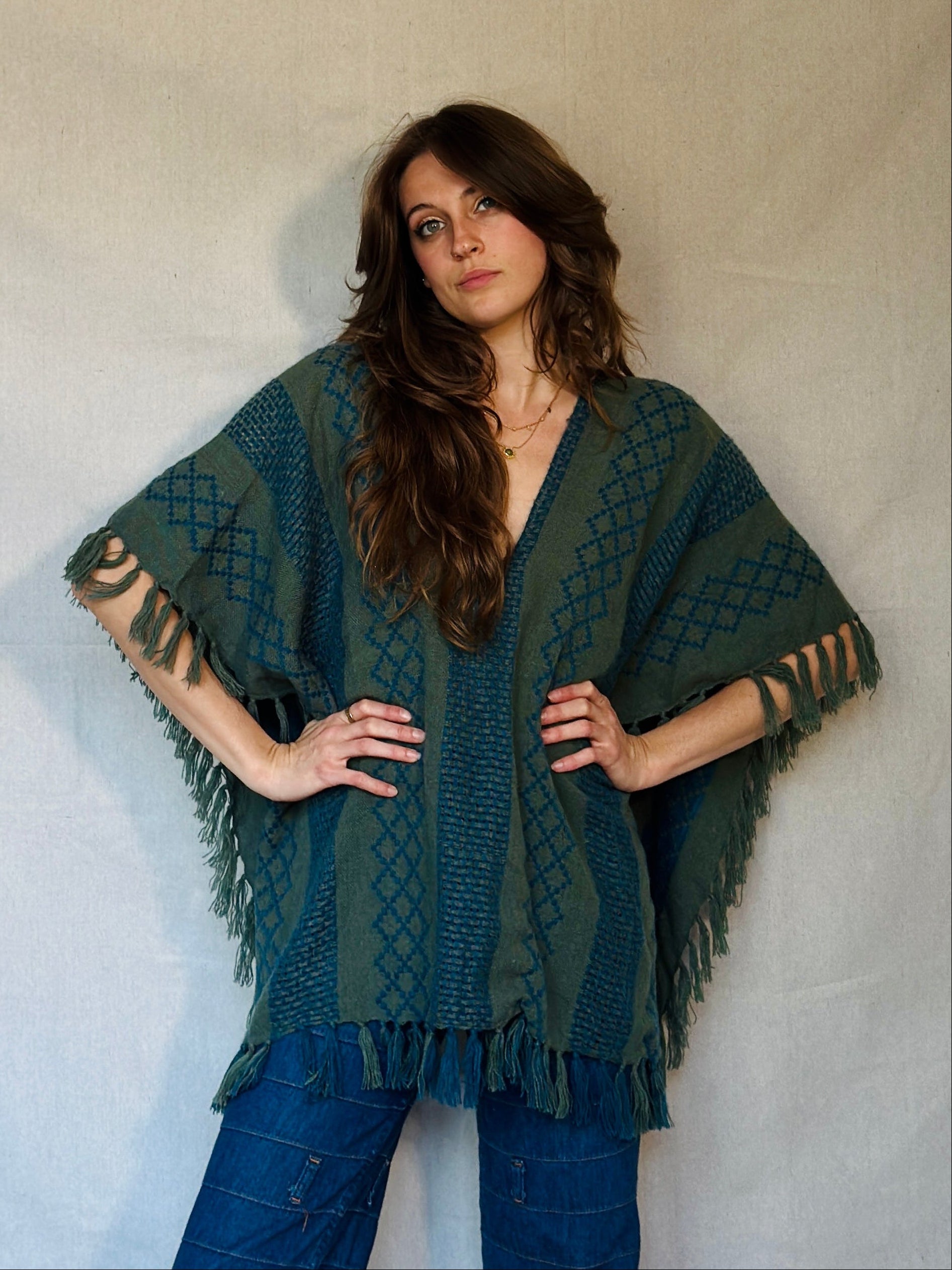 Woman wearing a green patterned poncho and blue pants against a white background
